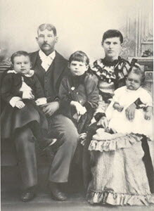 Black-and-white studio portrait of William Webster Bates and Florence Arminda 'Minnie' Staggs with three young children — a toddler on William's lap, a young boy standing between them, and an infant in Minnie's arms.