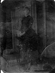 Faded, low-contrast tintype photograph, believed to be Minnie Staggs, seated in formal pose; facial features and clothing details are difficult to discern due to the age and condition of the original.