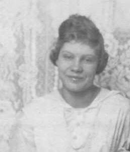 Black-and-white studio portrait of a young Alice Josephine Davis, hair swept up and pinned, wearing a light-colored blouse with a soft collar, smiling gently against a patterned studio backdrop.
