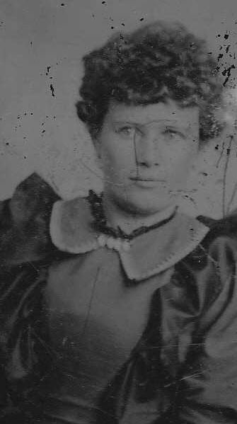 Black-and-white portrait of a young Annie E. Chaney, cropped from a larger tintype. She has curly hair swept up and back, and wears a dark dress with a light fur or ruffled trim collar. The original tintype shows scattered dark speckling and surface wear.