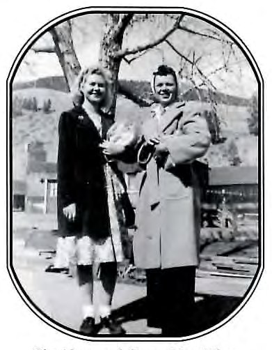 Black-and-white photograph of a young woman and a young man standing together outdoors near a tree, both smiling.