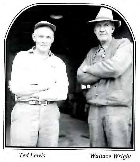 Black-and-white photograph of two men standing together with arms crossed in front of a building doorway.
