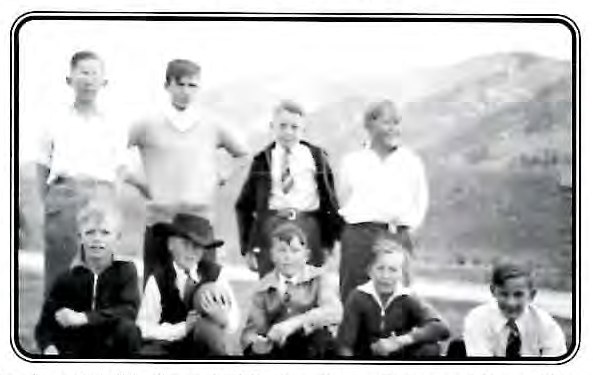 Black-and-white photograph of eight boys posed together outdoors on a hillside, four standing and four kneeling in front.