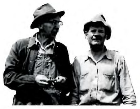 Black-and-white photograph of two men standing together outdoors wearing hats.