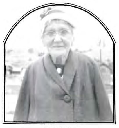 Black-and-white photograph of an older woman wearing a hat and coat, standing outdoors.