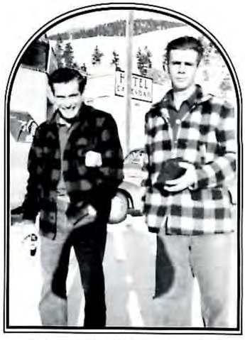 Black-and-white photograph of two young men standing together outdoors near parked cars.