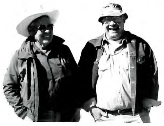 Black-and-white photograph of two men standing together outdoors wearing jackets and caps.