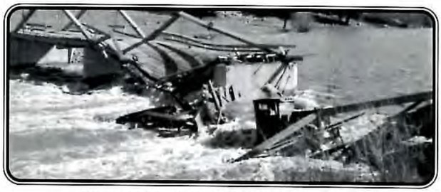 Black-and-white photograph of a collapsed steel truss bridge lying in a rushing river.