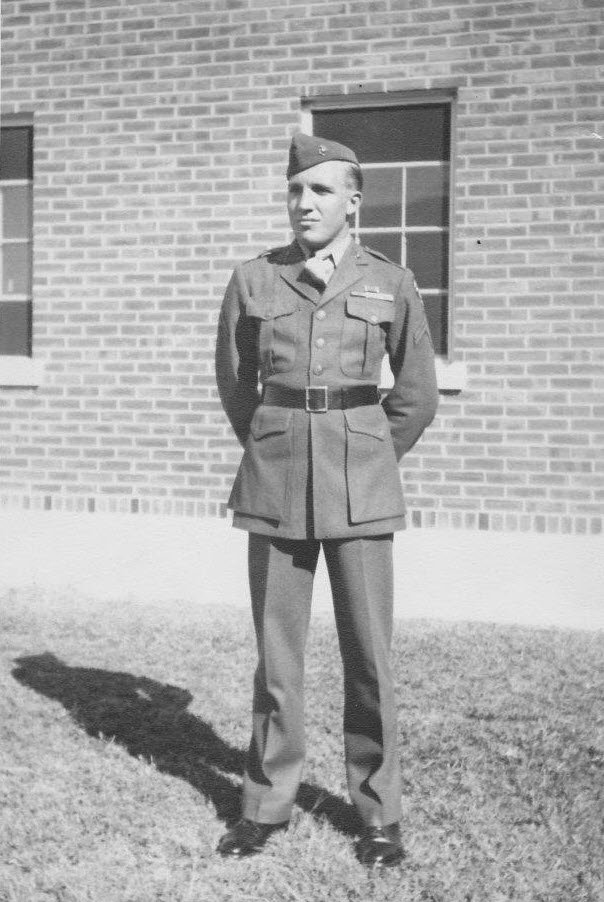 Joel Thomas Jackson standing outdoors in his U.S. Marine Corps dress uniform, hands clasped behind his back, in front of a brick building.