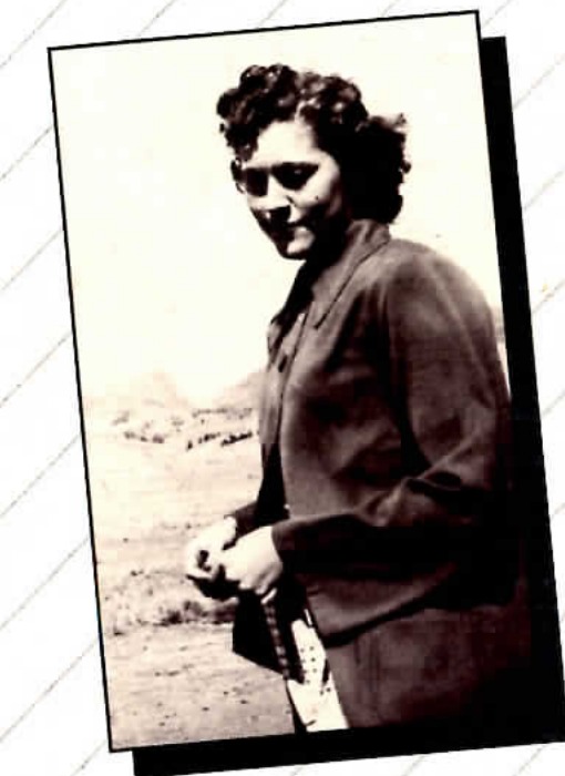 Black and white photograph of a young woman in a jacket standing outdoors, tinted sepia.
