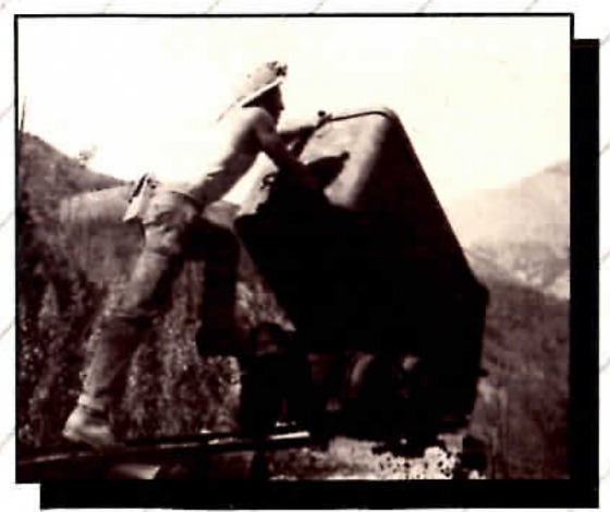 Black and white photograph of a man climbing onto mining equipment on a mountainside.