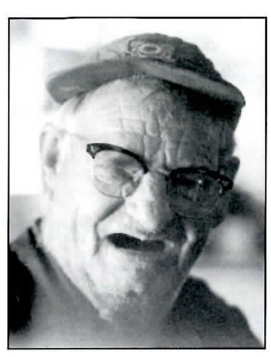 Black and white portrait photograph of an older man wearing a mining cap and glasses, smiling, printed above the tommyknocker poem.